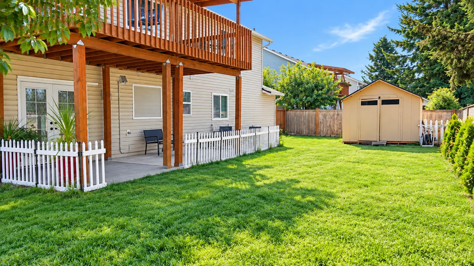 The back of Prime Adult Family Home showing a raised wooden deck, a shaded patio beneath it, a picket fence, and the garden