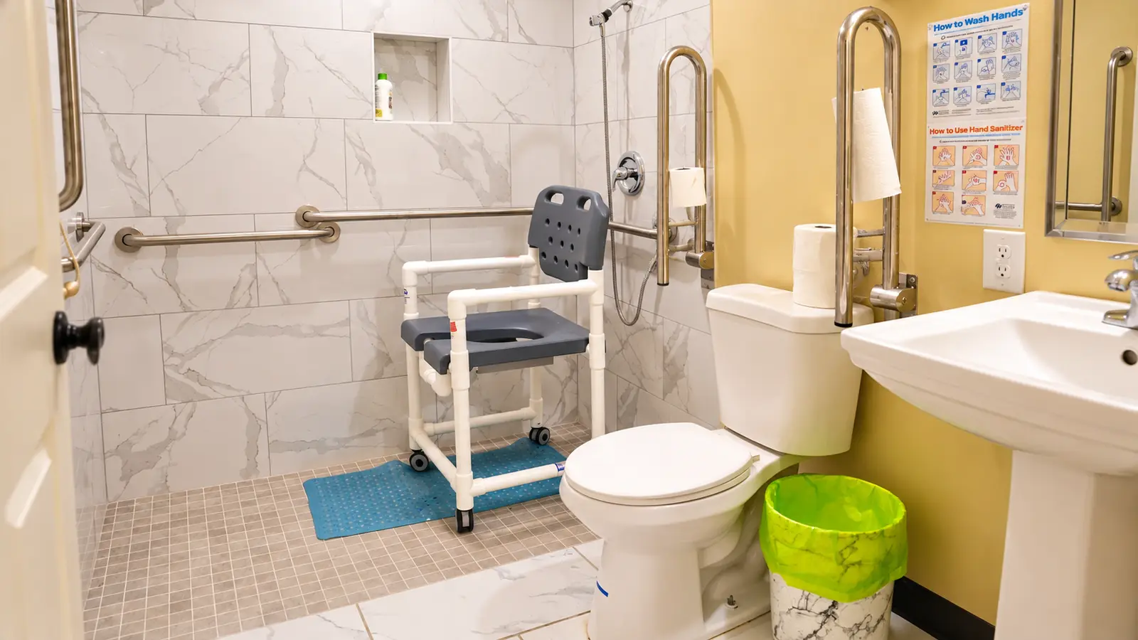 A roll-in shower at Prime Adult Family Home with grab bars, a hand-held shower, a non-slip mat, and a rolling shower chair
