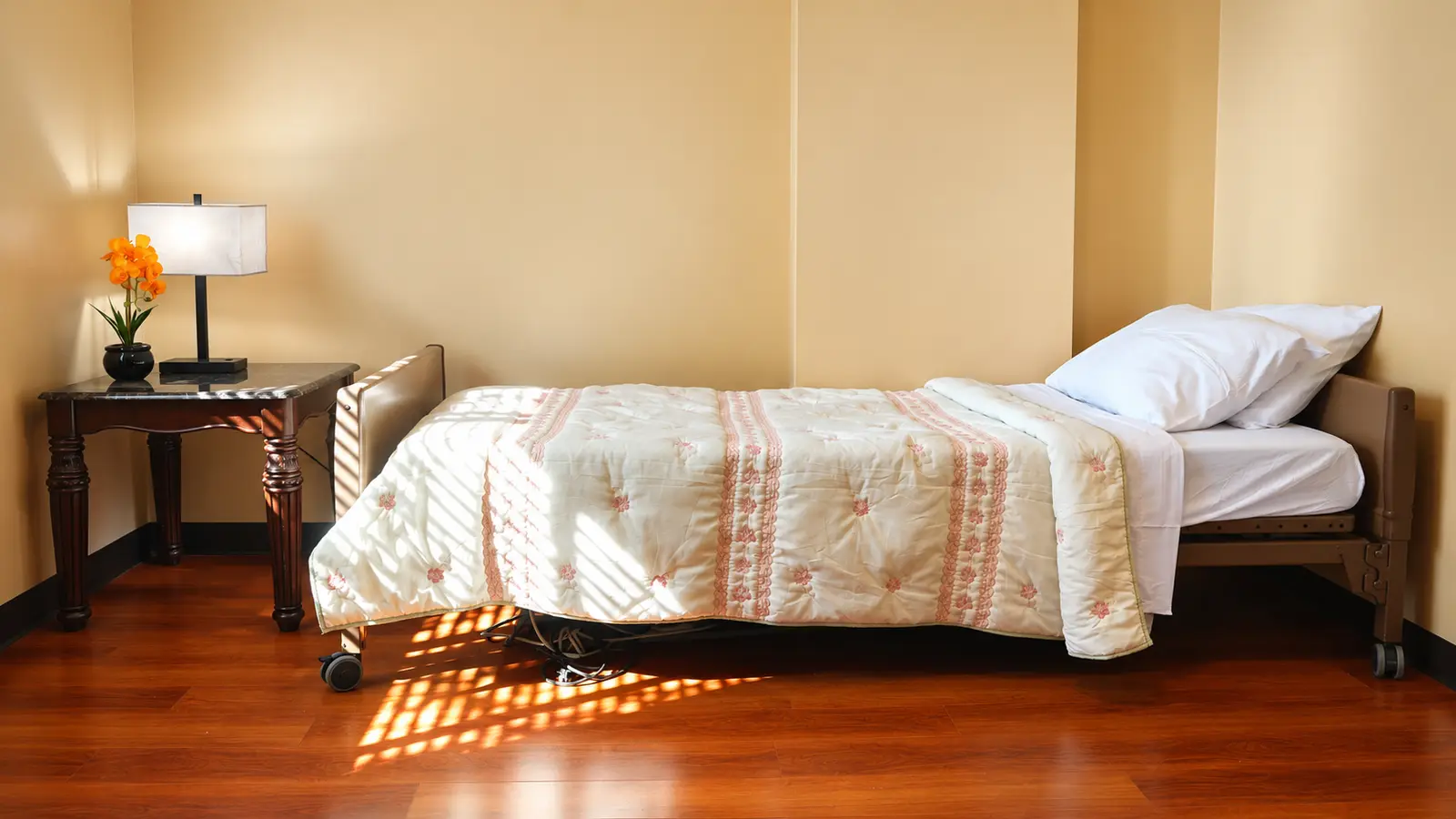 A resident bedroom at Prime Adult Family Home with an adjustable bed, a bedside table, a lamp, and afternoon light across the floor