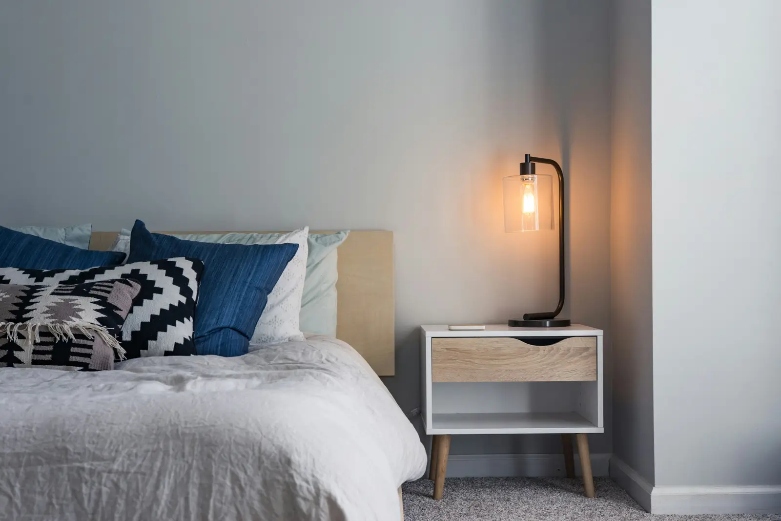 A neatly made bed beside a bedside table and a warm reading lamp