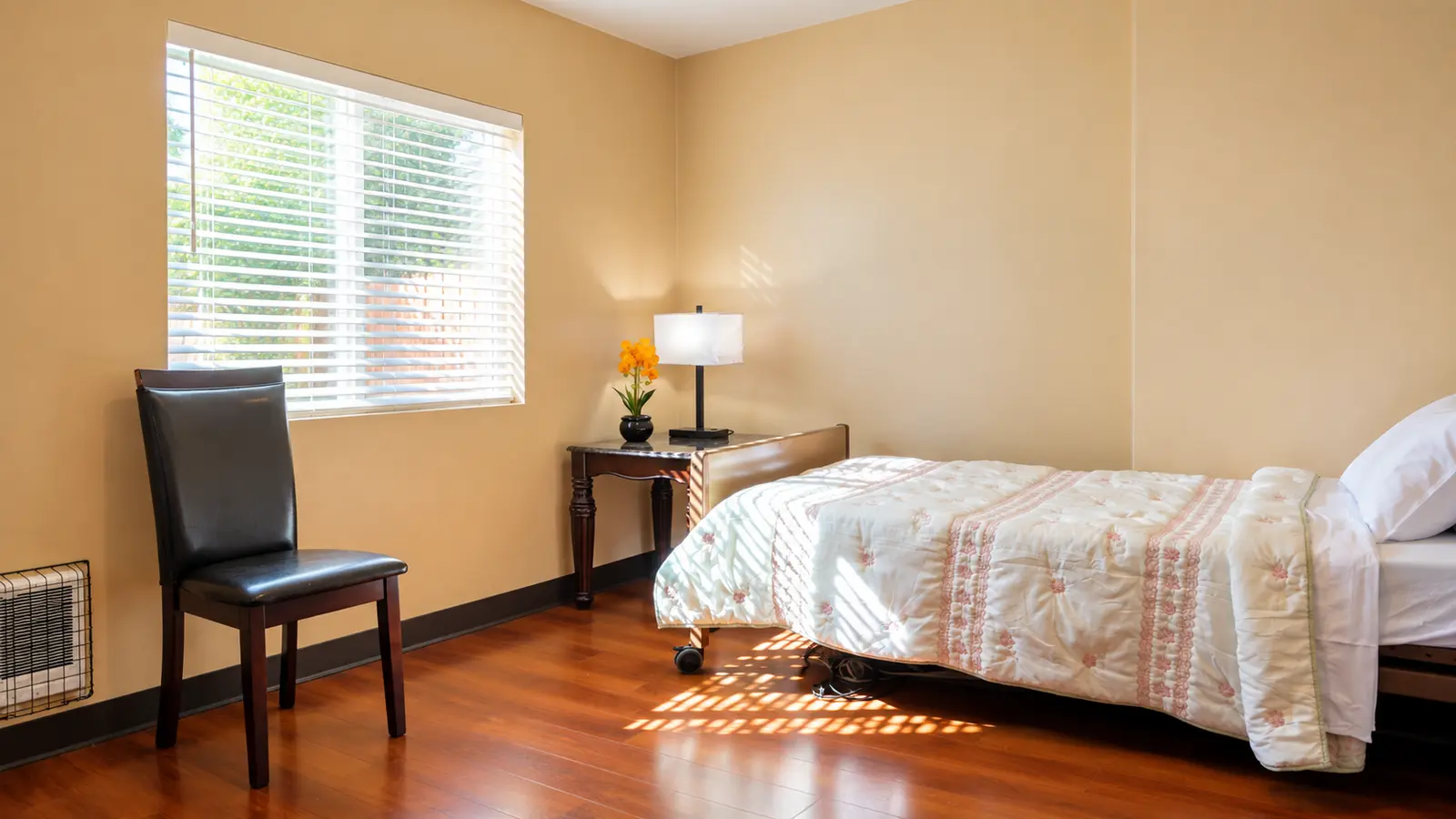 A resident bedroom at Prime Adult Family Home with a window, a chair, a bedside lamp, and a made bed