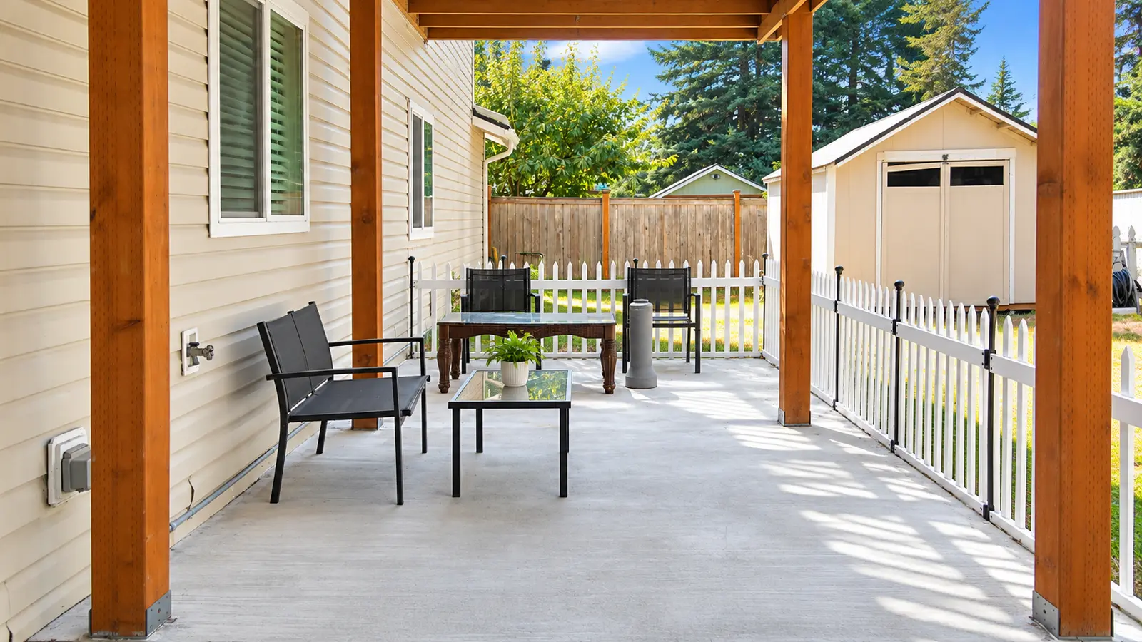 A covered patio at Prime Adult Family Home with outdoor chairs and a table, looking out to the fenced garden