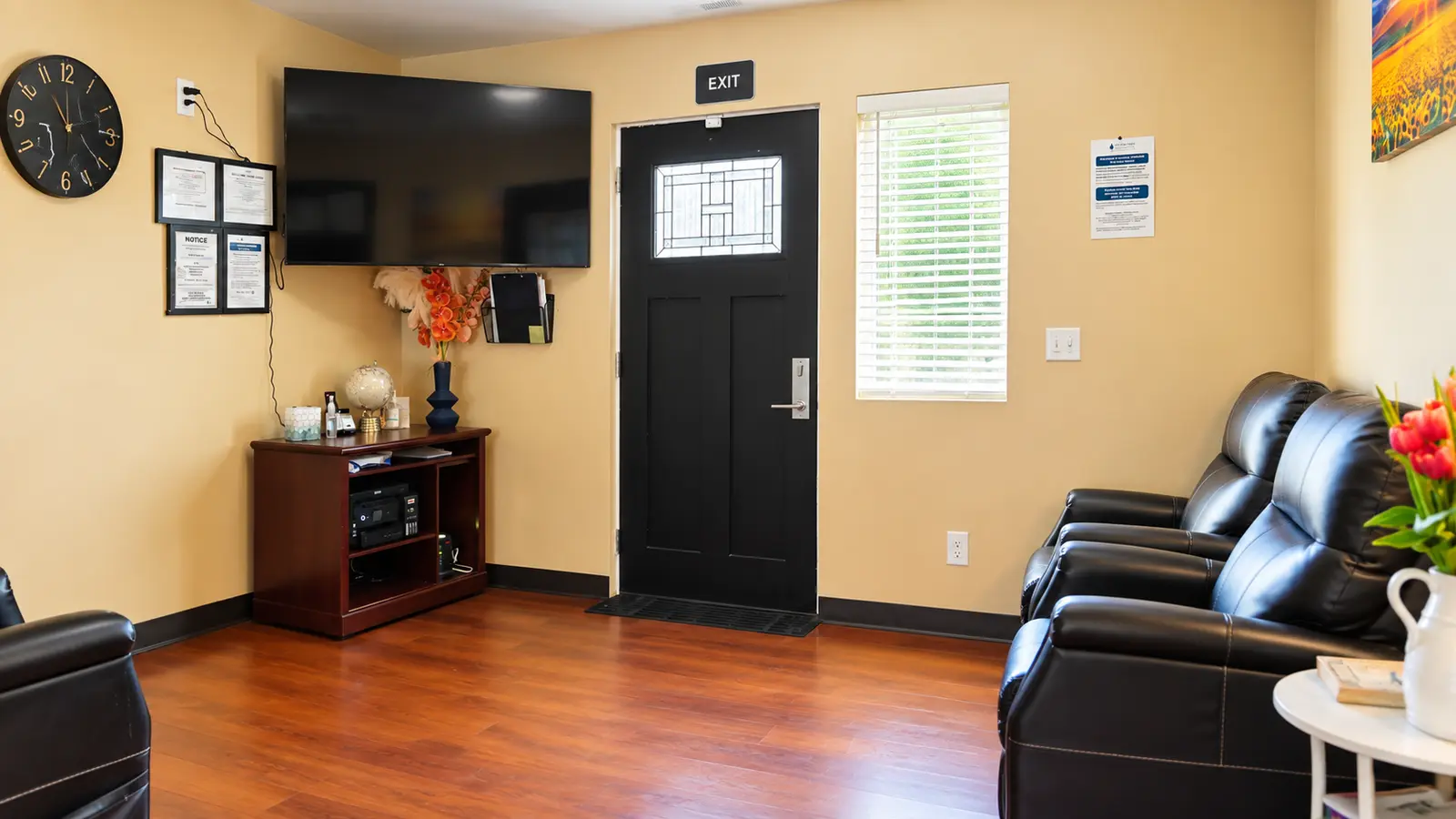 A sitting area at Prime Adult Family Home with reclining armchairs, a wall-mounted television, a clock, and the front door