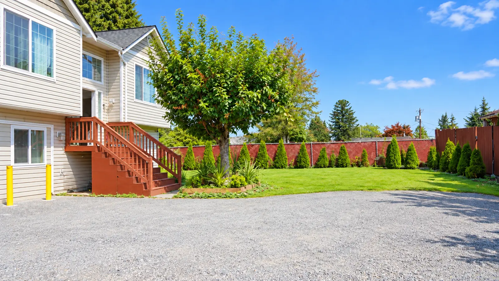The side of Prime Adult Family Home with its wooden entry stair, a young tree, lawn, and a fenced boundary