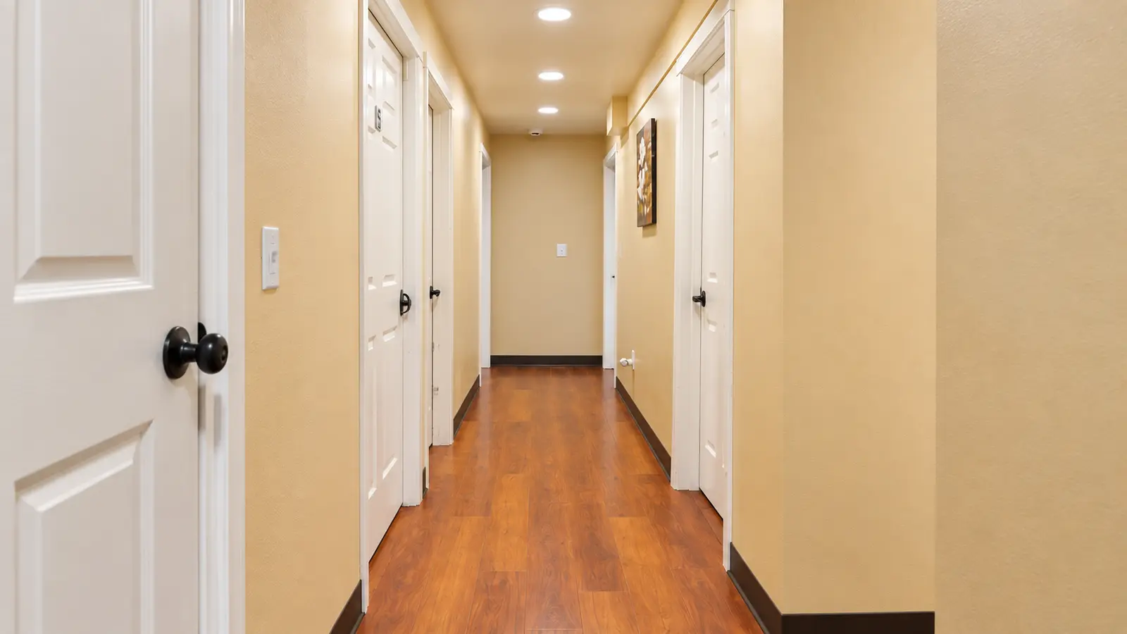 A wide interior hallway at Prime Adult Family Home with white doors along both sides and wood flooring