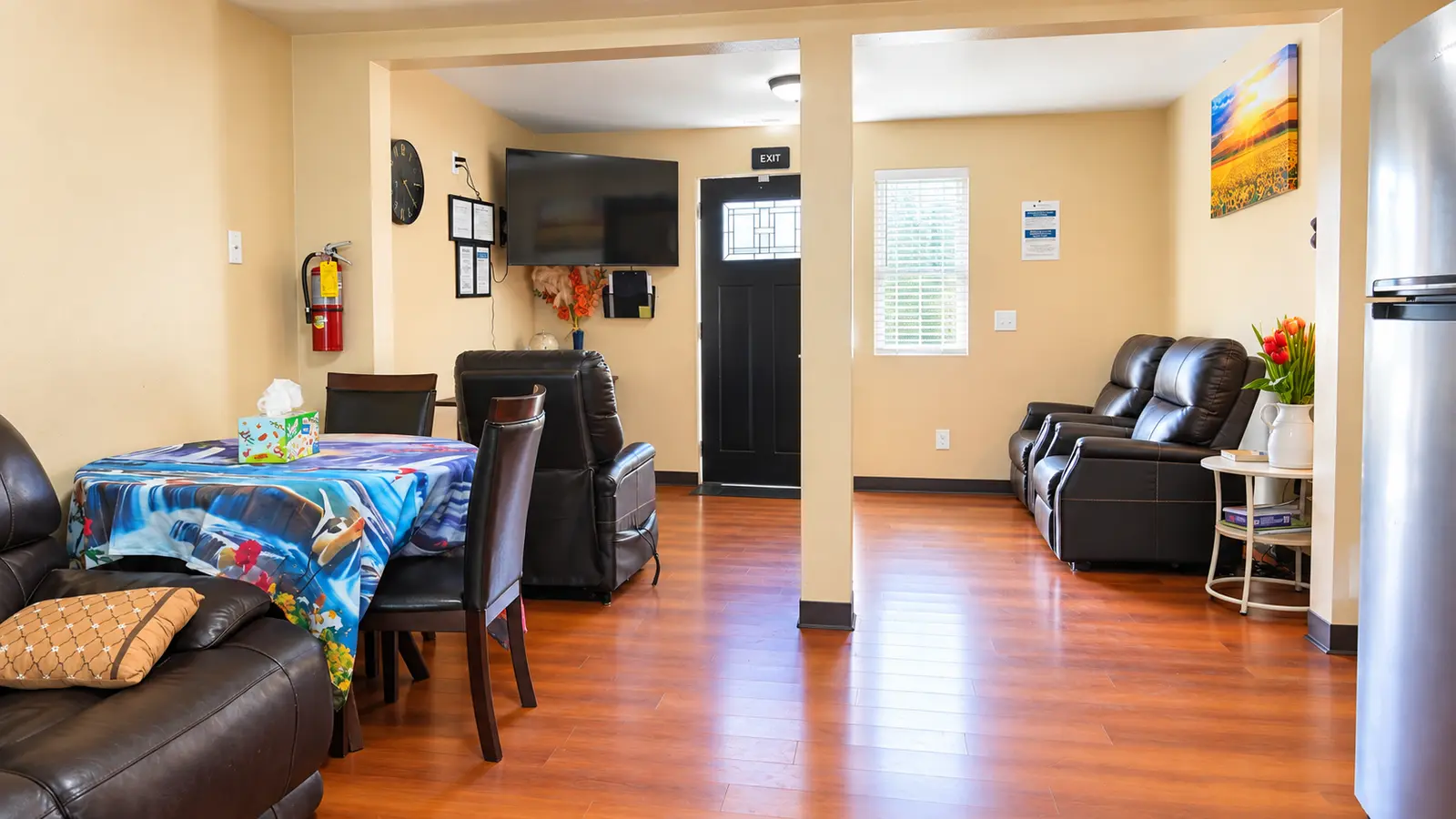 The open living and dining area at Prime Adult Family Home, with a dining table, armchairs, a sofa, and wood floors running through