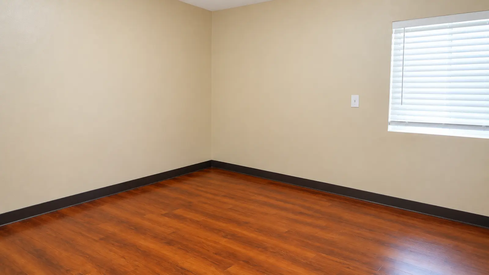 An unfurnished room at Prime Adult Family Home with a shuttered window and wood flooring